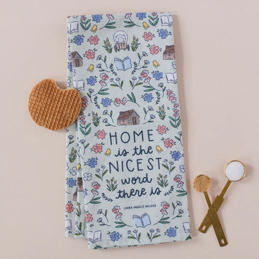 Photo with light pink bacground. A waffle with a bite mark and two measuring sppons full of sugar and brown sugar sit beside a tea towel. The tea towel has the the quote, "Home is the Nicest Word There Is" by Laura Ingalls Wilder. The towel has log cabins, covered wagons, and flowers decorating it. 