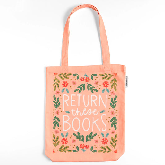 A peach-colored canvas tote bag with the text "RETURN these BOOKS" in a stylized white and light blue font, surrounded by a floral and leafy design in red, green, and pink.